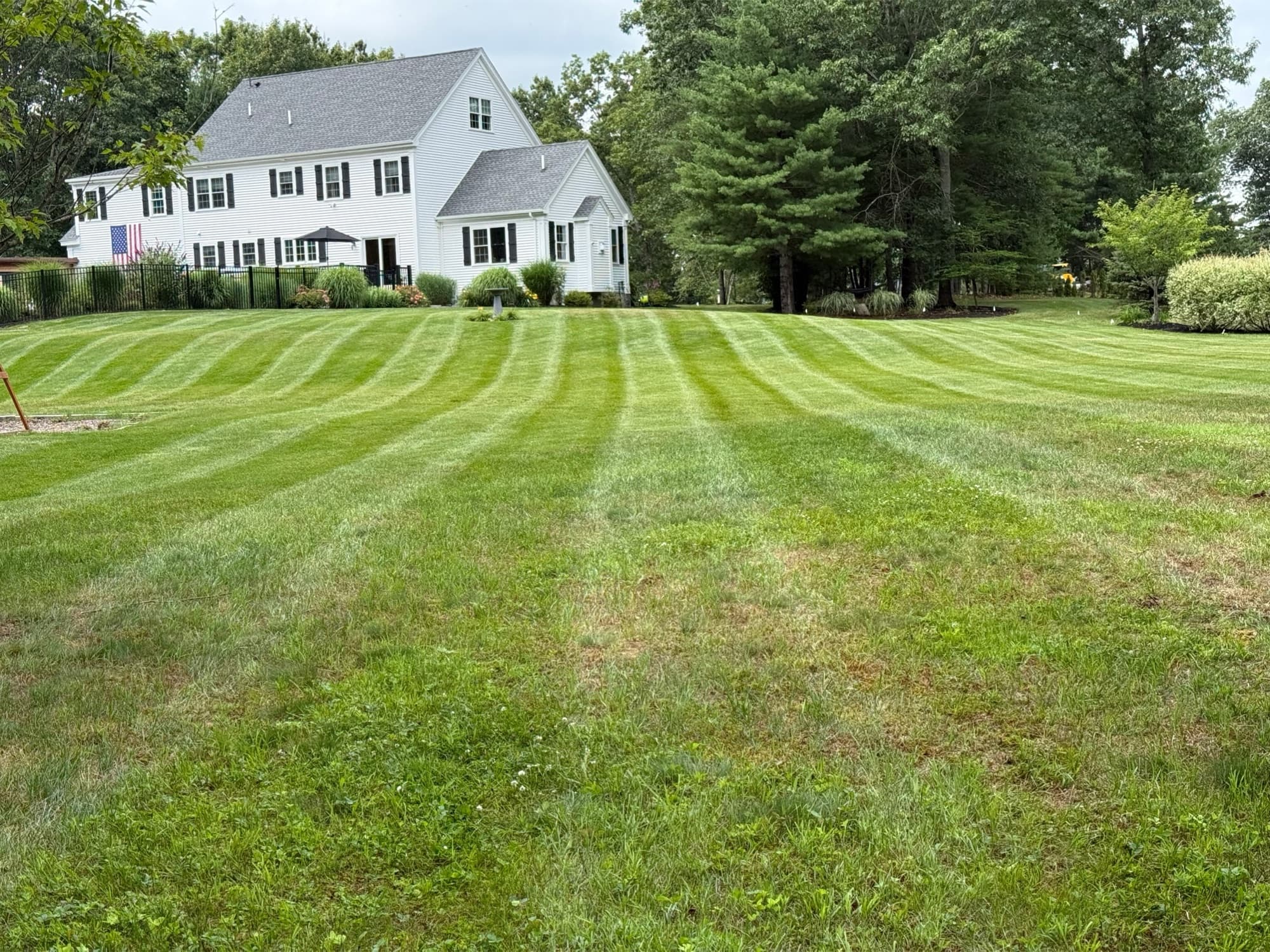 White colonial home behind a broad, freshly striped lawn