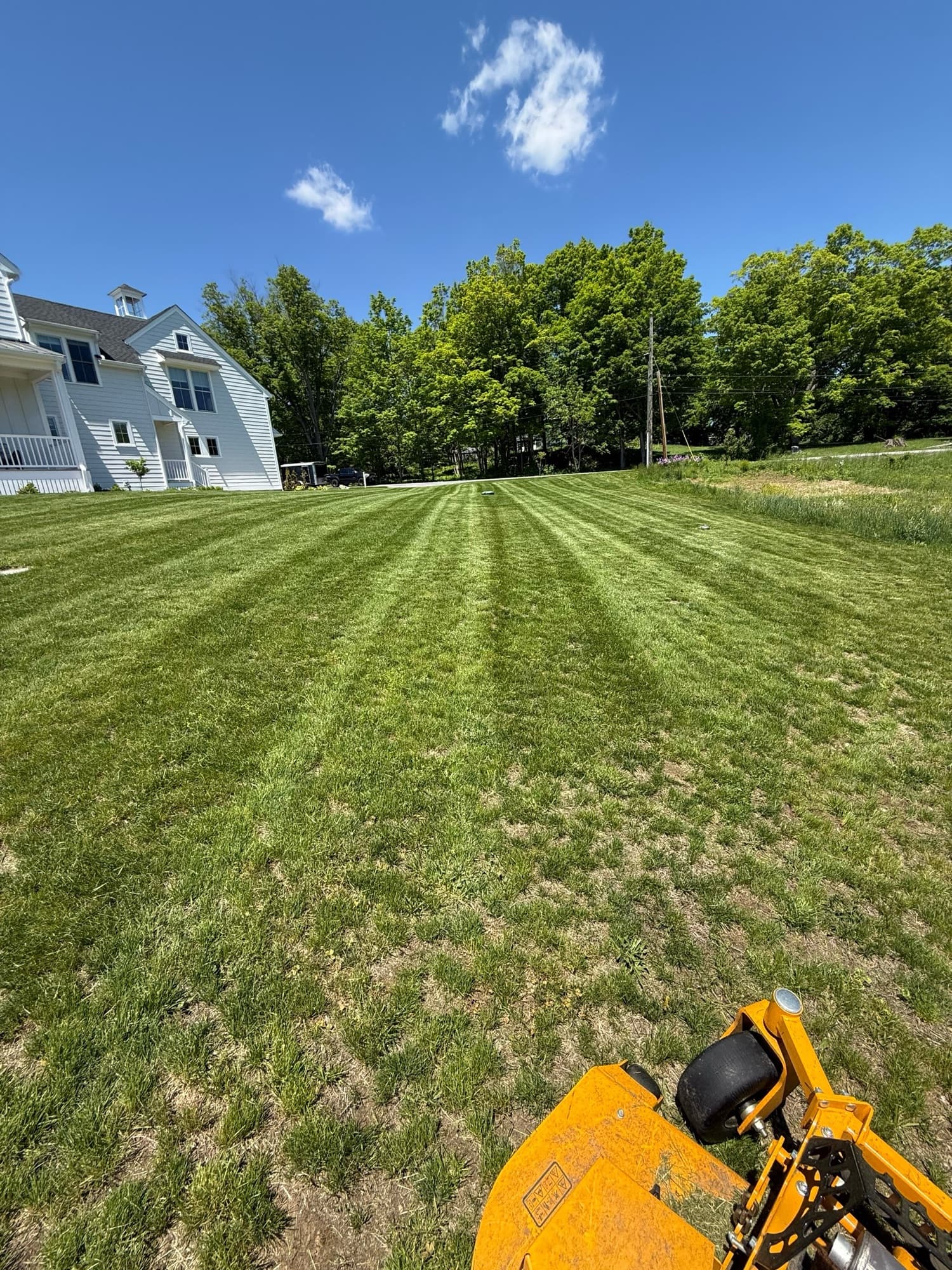 Mower on a broad green lawn beside a white farmhouse