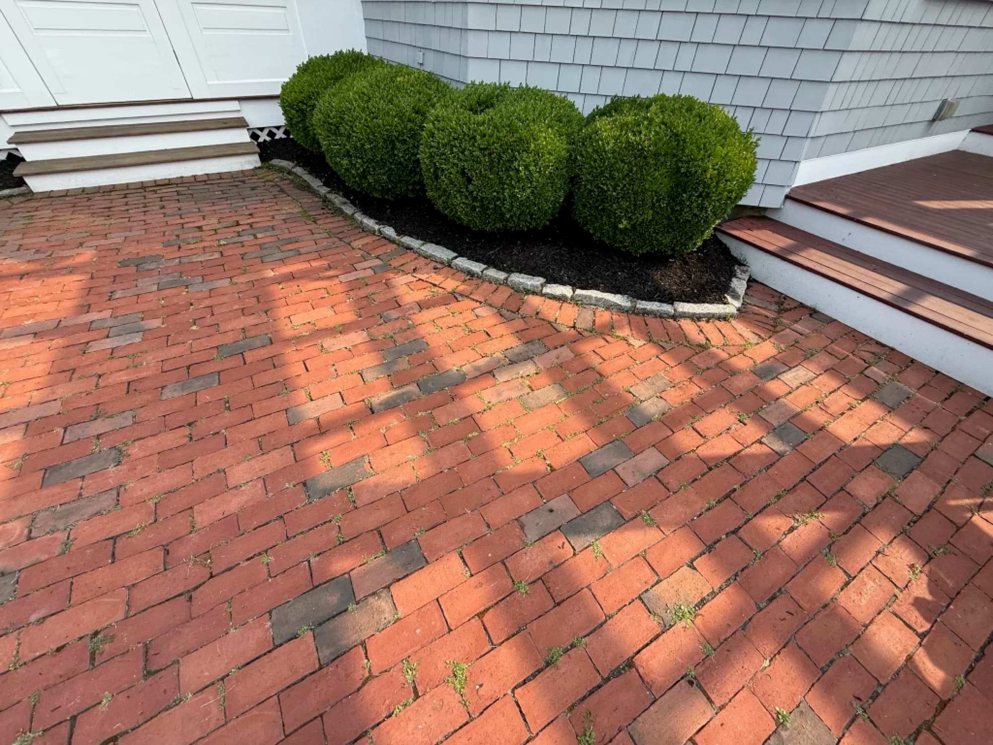 Trimmed boxwoods in a fresh mulch bed along a brick patio