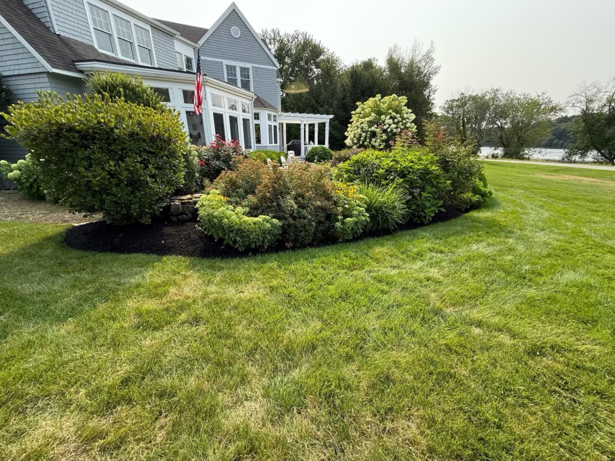 Freshly mulched beds wrapping a waterfront shingle-style home